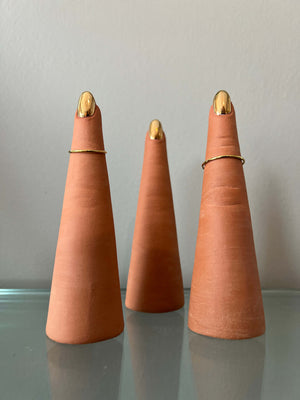 Each finger is made from terracotta clay and finished with a gold luster on the nail. Each finger can fit ring size 9 through 4.