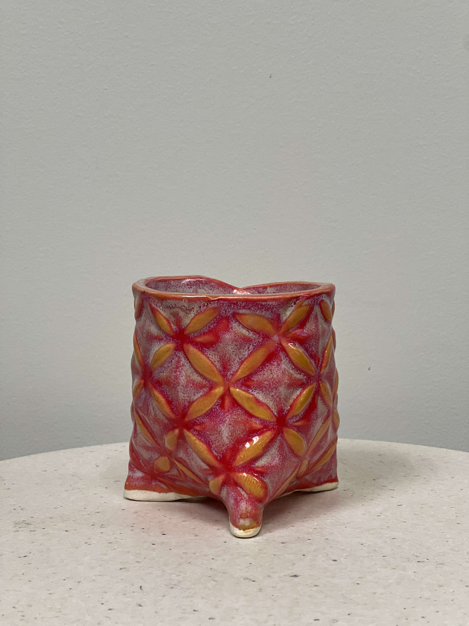 A hand formed pinch-pot planter with decorative reliefs and pink glaze.