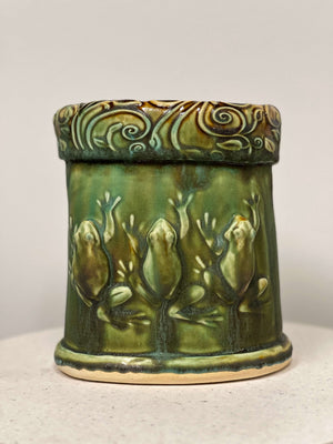 A hand formed planter with a trio of frogs in relief and moss green glaze with brown accents.