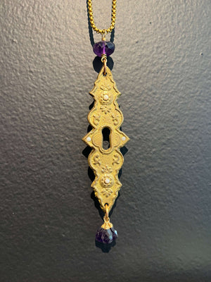 Antique cast brass escutcheon set with fire opals and embellished with amethysts hanging on 26” long brass box chain.