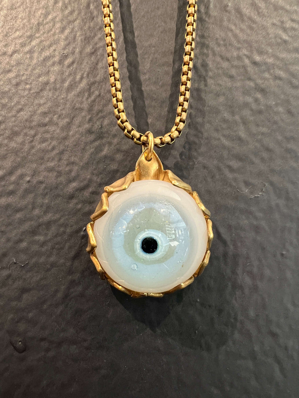 A medium handblown borosilicate glass eye caged in a vintage brass sunflower stamping and hanging on brass box chain.