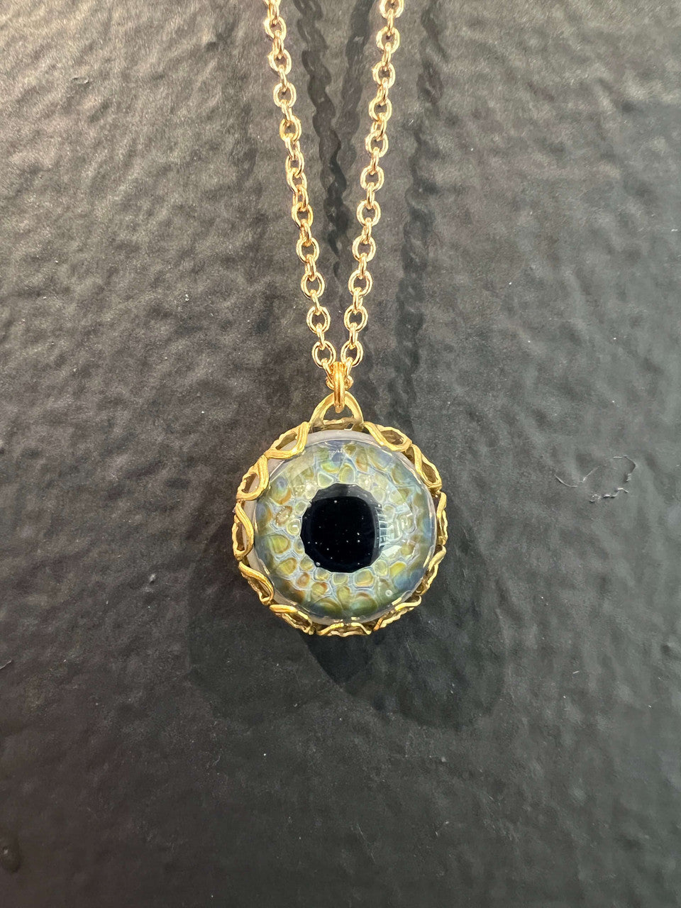 Handblown blue borosilicate glass eye caged in vintage brass filigree and hanging on a brass chain.