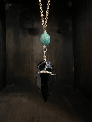 An Obsidian arrowhead paired with Elisa Turquoise accent hanging an 18” long brass satellite chain with a gold filled spring ring clasp.